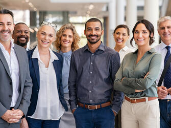 Portrait of successful group of business people at modern office looking at camera. Portrait of happy businessmen and satisfied businesswomen standing as a team. Multiethnic group of people smiling and looking at camera.